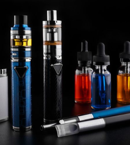 Modern electronic cigarettes and bottles with assorted vape liquid on black background
